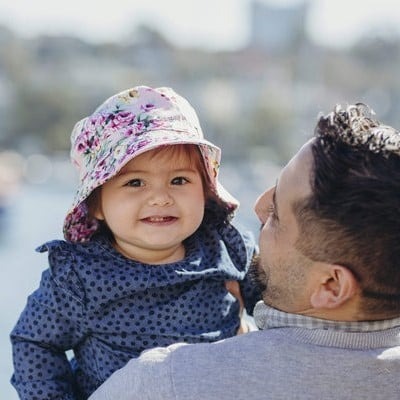 fetita cu palarie model floral banz sta in bratele tatalui si zambeste