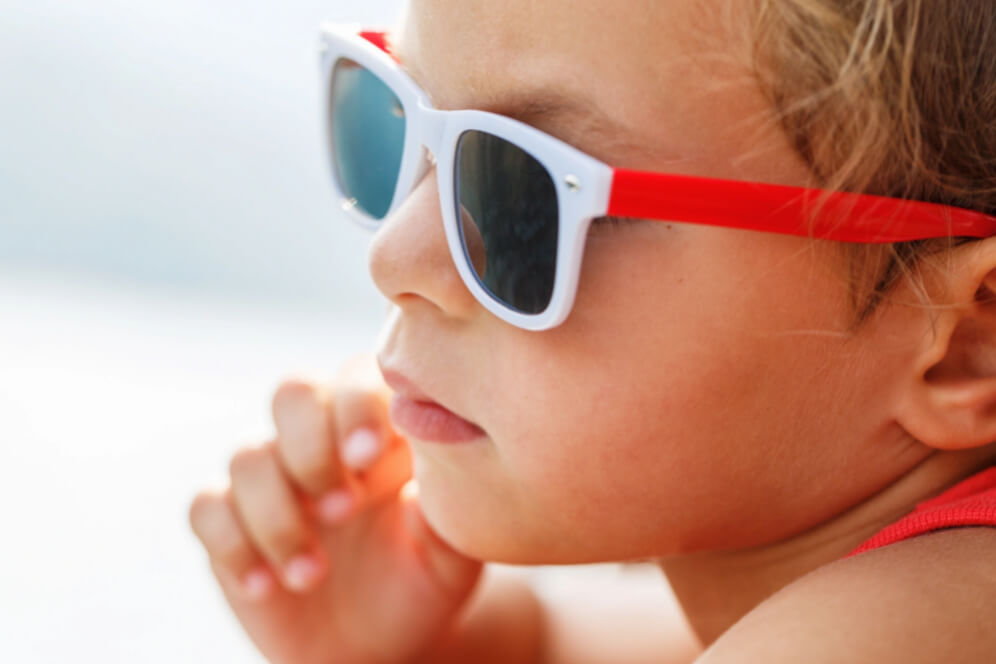 profil de baietel cu ochelari de soare cu rama alba si rosie pe ochi